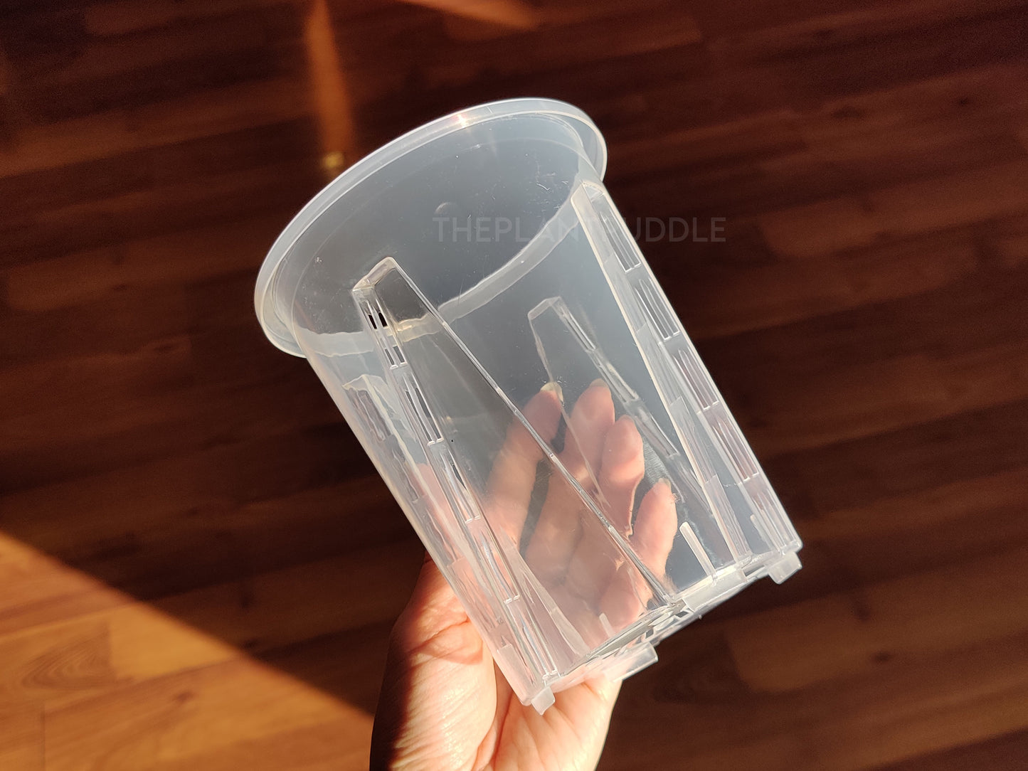 hand holding tall clear pot, showing side drainage holes
